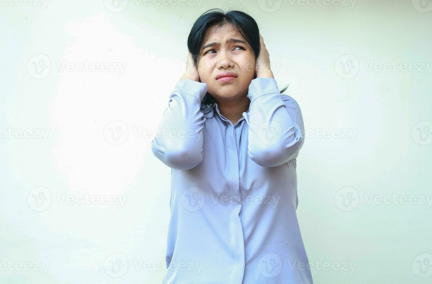 assustado ásia mulher cobertura orelhas apavorado tocante cabeça vestido dentro formal terno olhando ausente, isolado em branco fundo foto