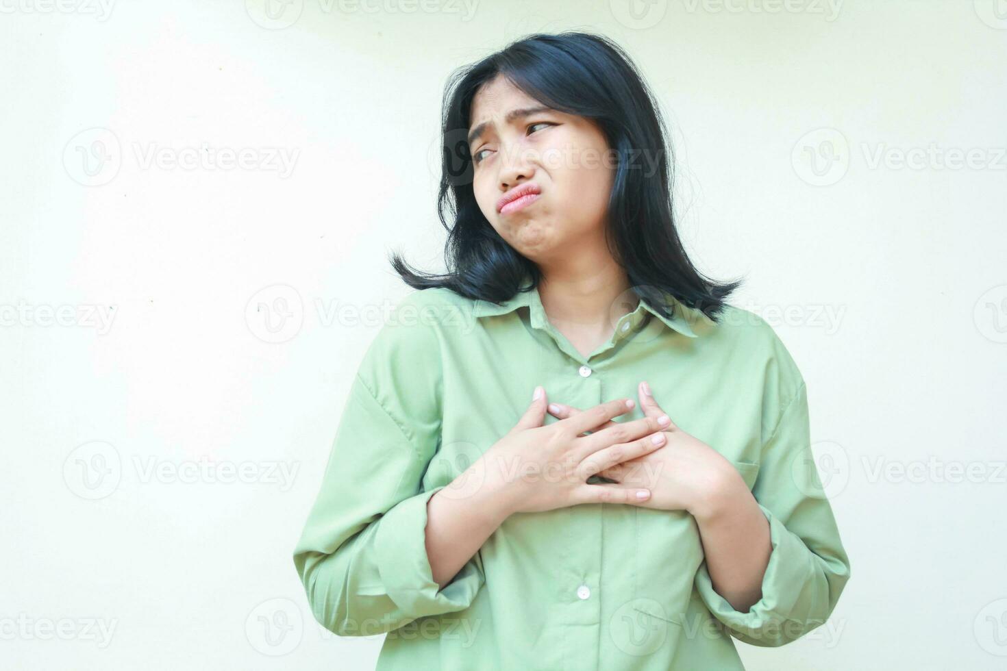 triste ásia mulher com Sombrio cabelo vestindo verde camisa olhando a parte, de lado para esvaziar espaço com preocupação face expressão ter pensar demasiado e ansiedade, em pé sobre isolado branco fundo foto