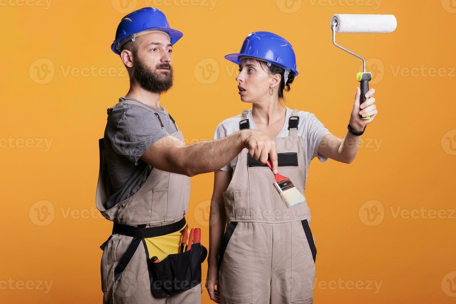 jovem construção trabalhadores posando com pintura ferramentas, em pé sobre amarelo fundo. equipe do construtores segurando pincel e rolo escova para trabalhos em reforma projeto dentro estúdio. foto