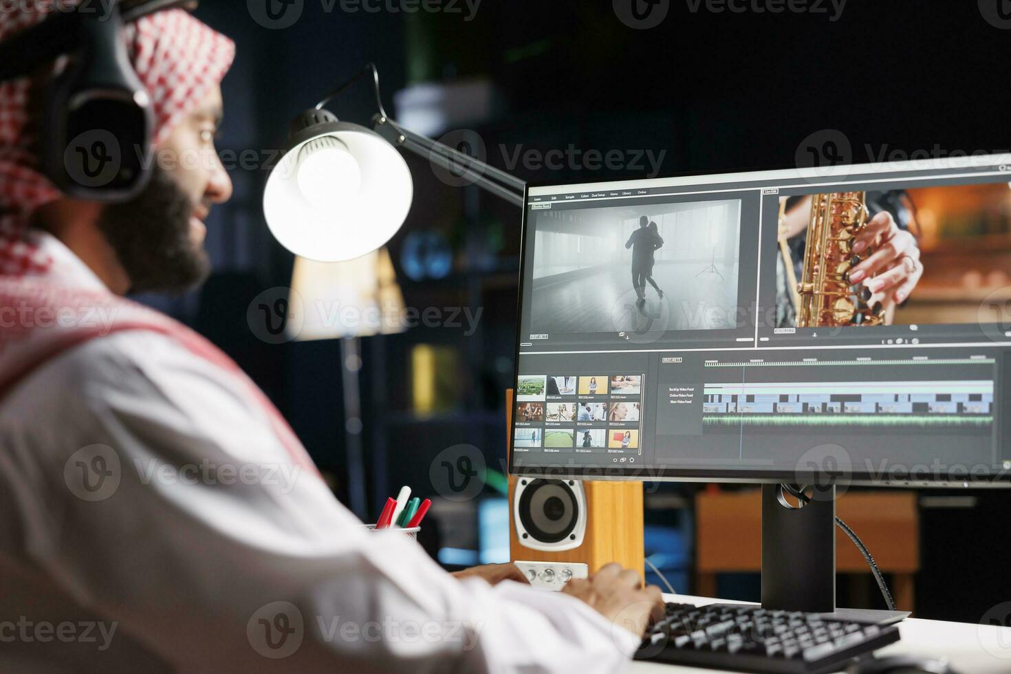 árabe masculino cineasta sentado às mesa diligentemente trabalhando em postar Produção para filme. muçulmano vídeo editor dentro tradicional traje, vestindo sem fio fones de ouvido enquanto examinando cenas em computador tela. foto