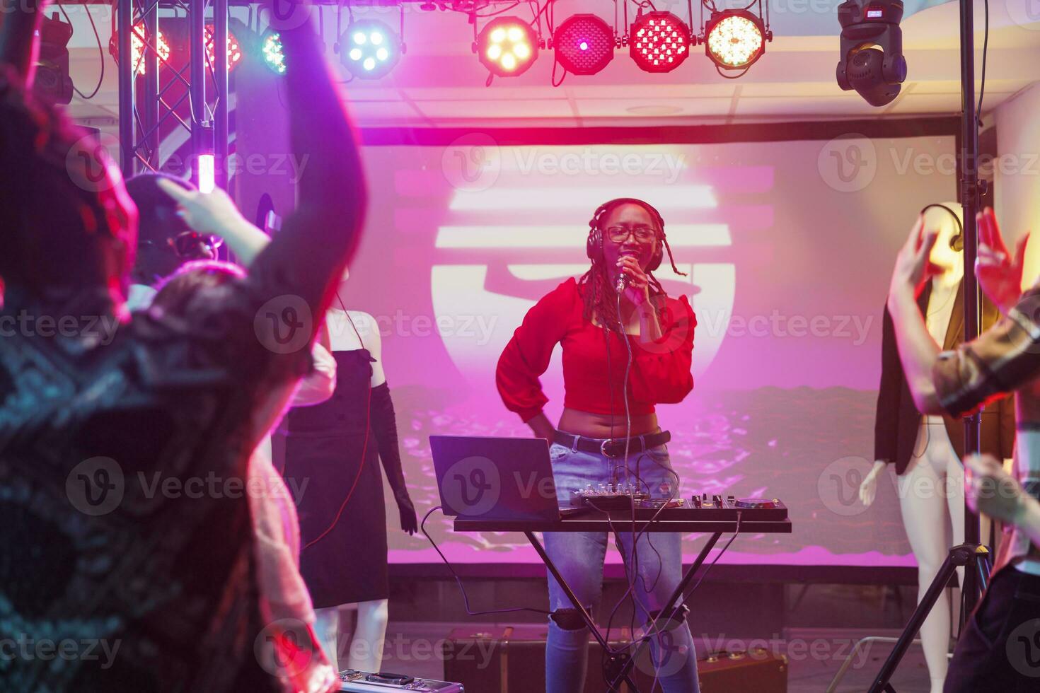 músico cantando e jogando eletrônico música em etapa dentro Boate. africano americano mulher dj usando microfone e som controlador equipamento enquanto realizando dentro lotado clube foto