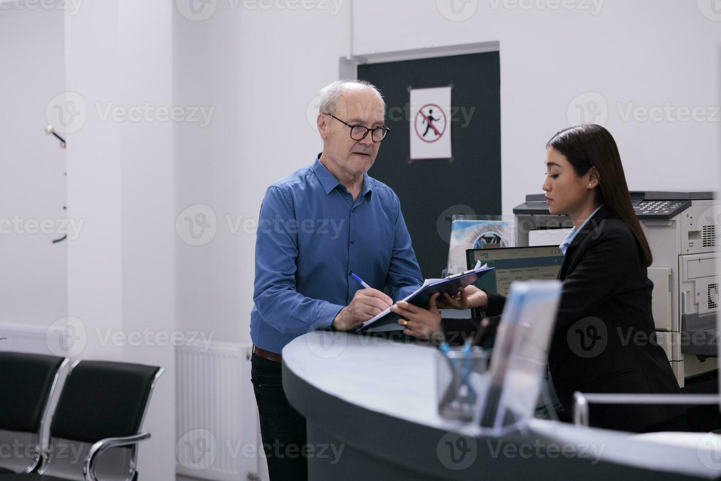 idosos paciente discutindo doença perícia com ásia recepcionista enquanto assinatura médico papel, em pé às hospital contador dentro hospital esperando área. saúde Cuidado serviço e conceito foto