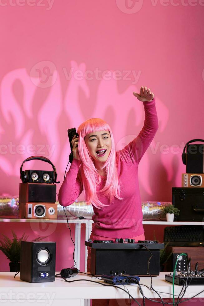 ásia artista com Rosa cabelo dançando e tendo Diversão dentro clube enquanto jogando techno música às profissional misturador console, desfrutando noite estilo de vida. artista fazendo desempenho com audio equipamento foto