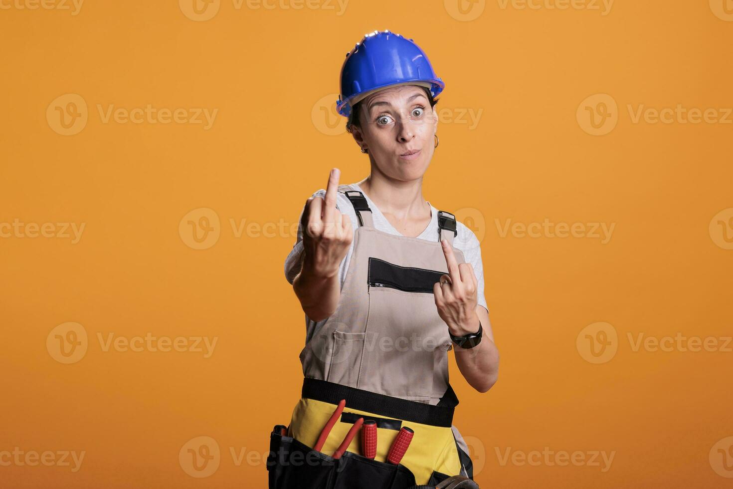 Bravo fêmea construtor mostrando meio dedo dentro estúdio, fazendo grosseiro gesto e agindo agressivo. fazer desaprovando sinais e expressando negativo emoção, descontente faz-tudo. foto