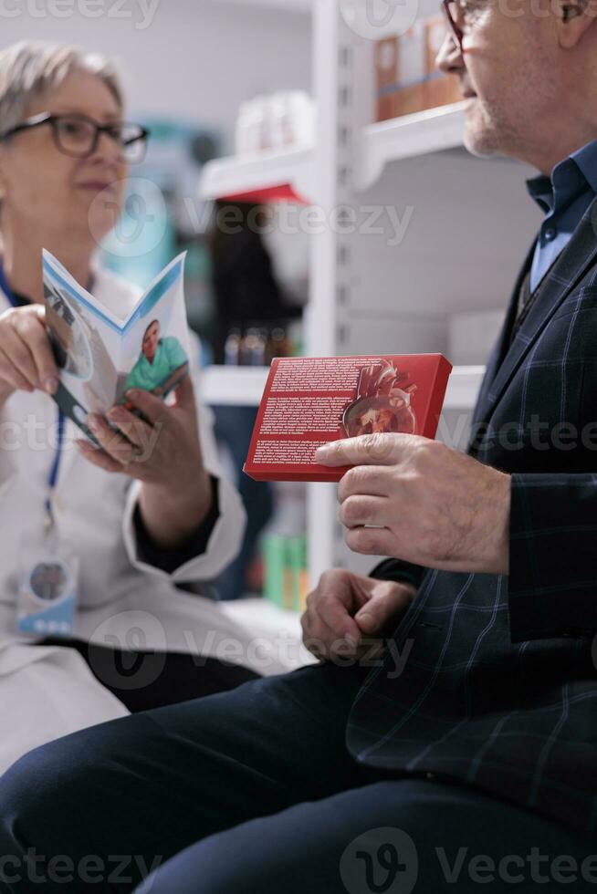 Senior mulher farmacêutico especialista dando cliente farmacêutico consultoria serviço, lendo paciente médico folheto sobre idosos saudável estilo de vida. velho homem segurando coração suplementos dentro farmácia foto