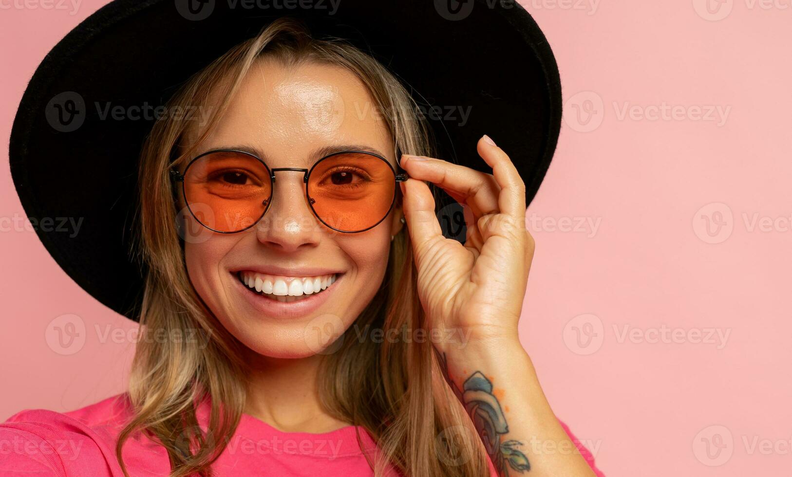 fechar acima estúdio foto do sorridente jovem mulher com tatuagem em mãos posando sobre Rosa fundo.