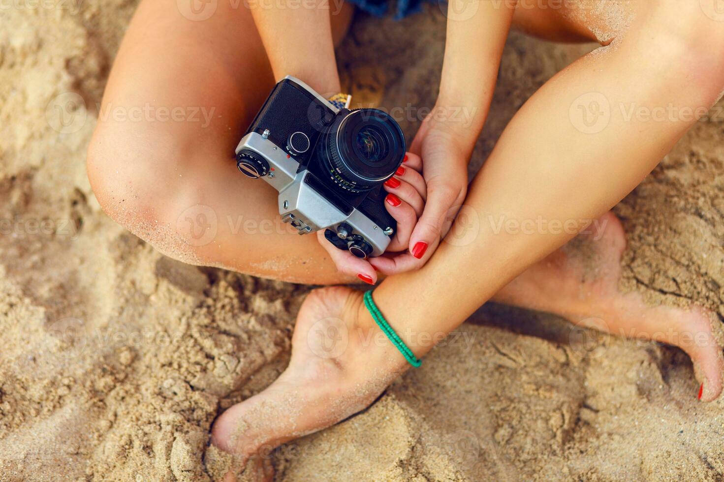 jovem senhora sentado em a tropical caloroso de praia a segurando retro câmera.mãos fechar-se. foto