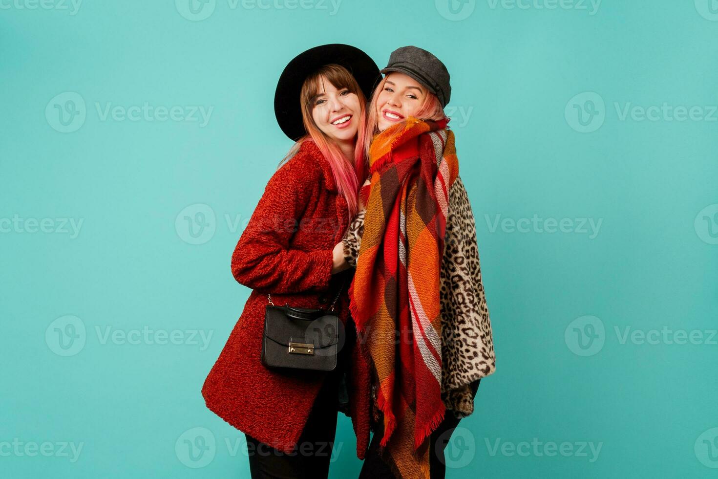 dois à moda loiro mulheres posando dentro estúdio em azul turquesa fundo. amigos abraçando e tendo Diversão junto. vestindo leopardo impressão falso pele casaco e lã lenço. inverno moda. foto