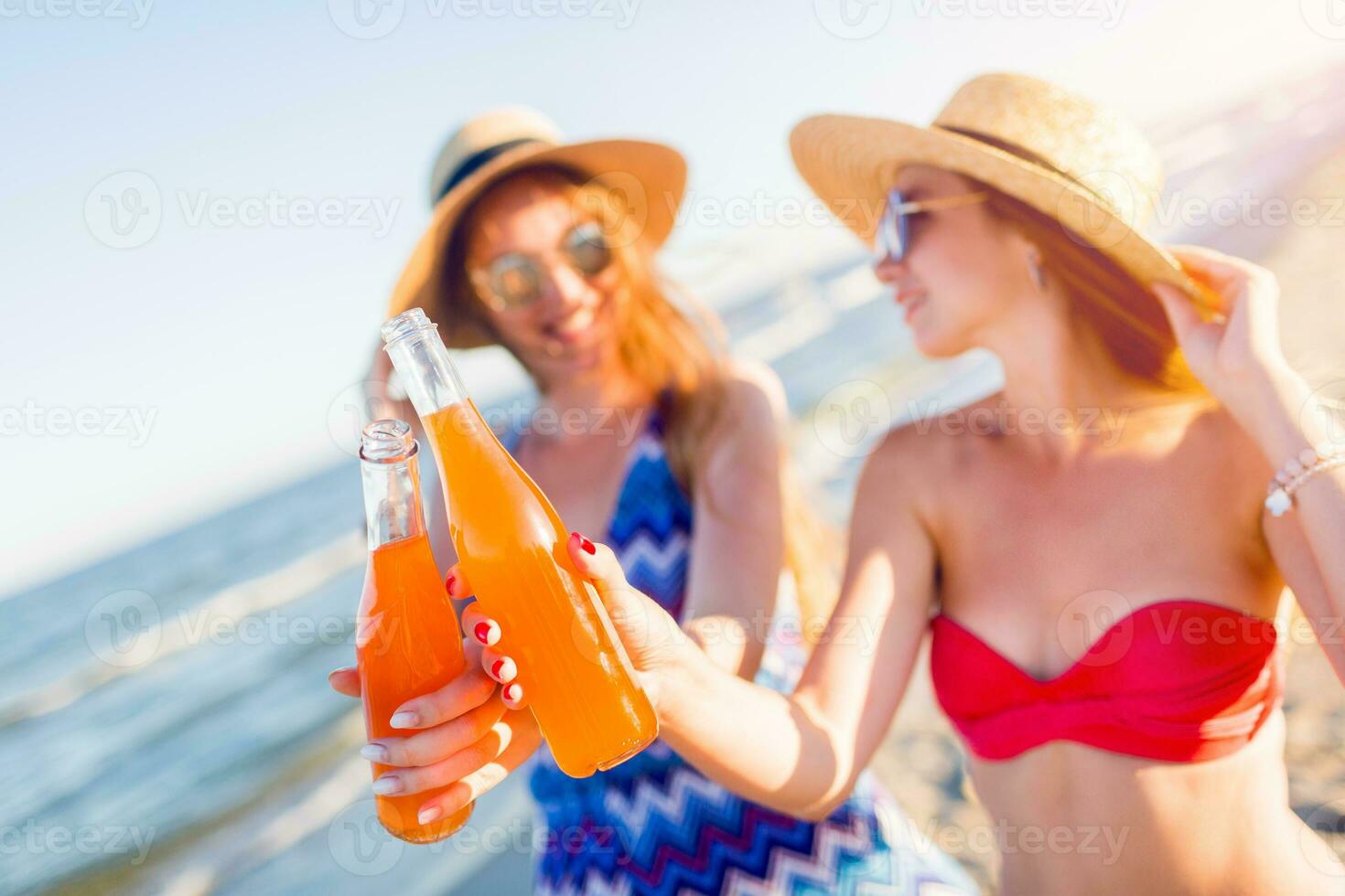 feliz amigos bebendo juntos em de praia com foco em garrafa desfrutando pôr do sol. festa tempo. foto