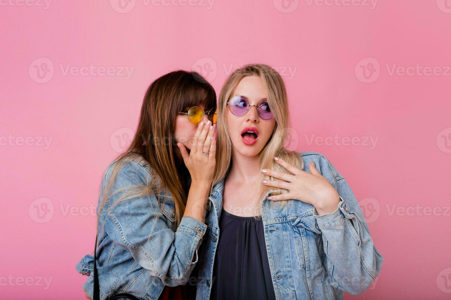 dois emocional meninas fofoca acima em Rosa fundo . Loiras mulher com surpresa face ouvindo dela morena amigo. foto