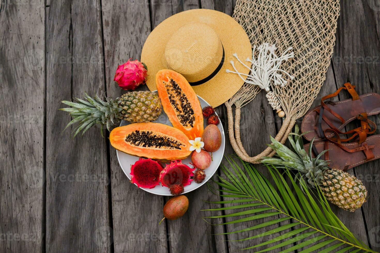 verão tropical composição. verde Palma folhas e tropical frutas em madeira fundo. plano deitar, topo visualizar. Palha chapéu e crochê tecido bolsa. foto