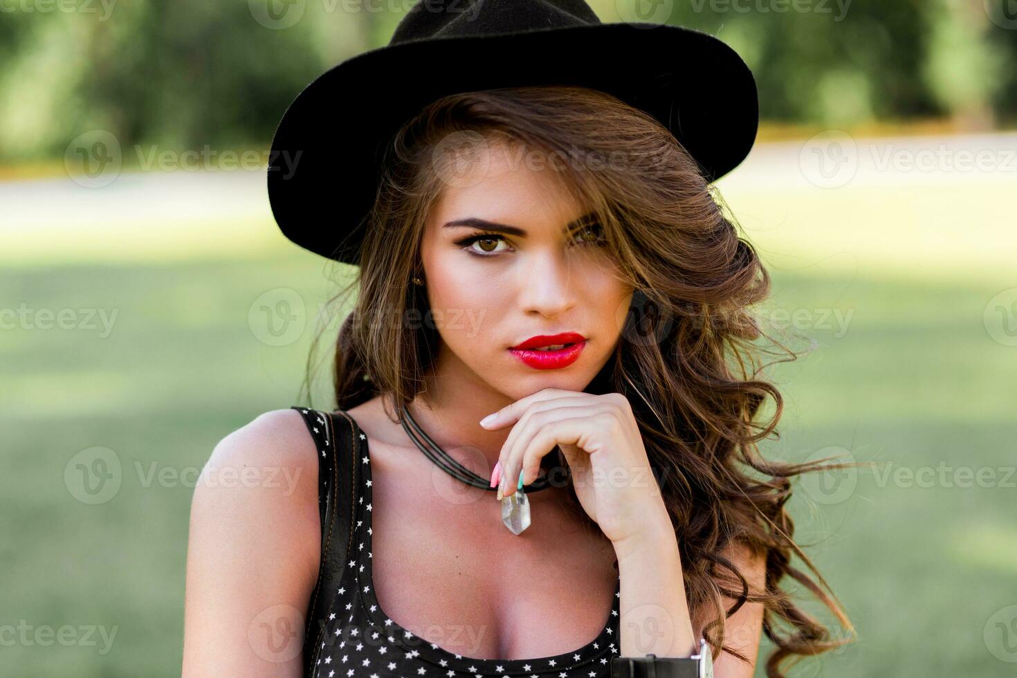 verão moda retrato do r elegante mulher com perfeito ondulado cabelo dentro à moda elegante Preto chapéu e brilhante faço acima posando dentro a parque. rua estilo. foto