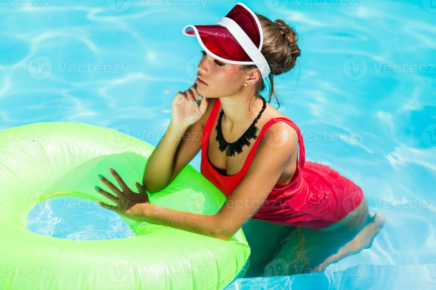 sexy bronzeada mulher dentro vermelho roupa de banho tendo Diversão e desfrutando verão dentro surpreendente grande natação piscina. jovem bonita menina natação em inflável anel. à moda transparente boné. de praia Festa. foto
