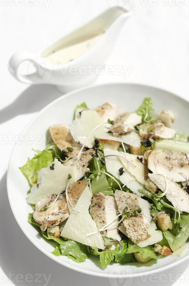 Salada Caesar de frango orgânico com queijo parmesão e croutons no fundo da mesa branca foto