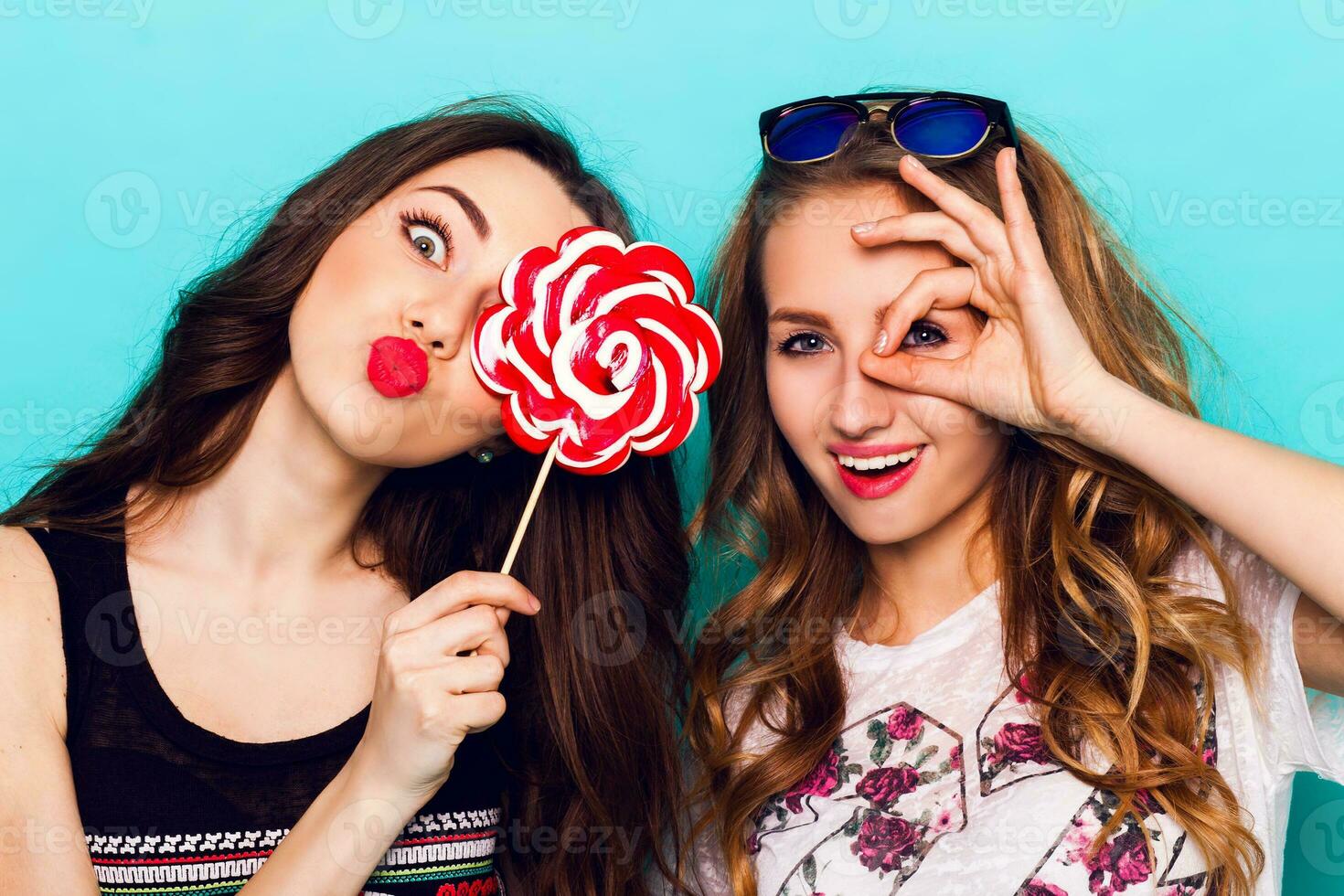 fechar op moda retrato do dois amigos ter Diversão , faço caretas ,diversão emoções e mostra a mão sinais. bonita meninas vestindo verão roupas e posando contra azul muro. foto