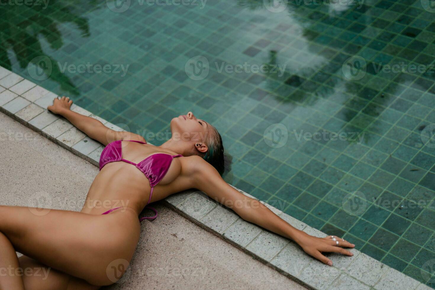 linda loiro mulher dentro sensual Rosa roupa de banho posando perto piscina em luxo tropical vila. foto