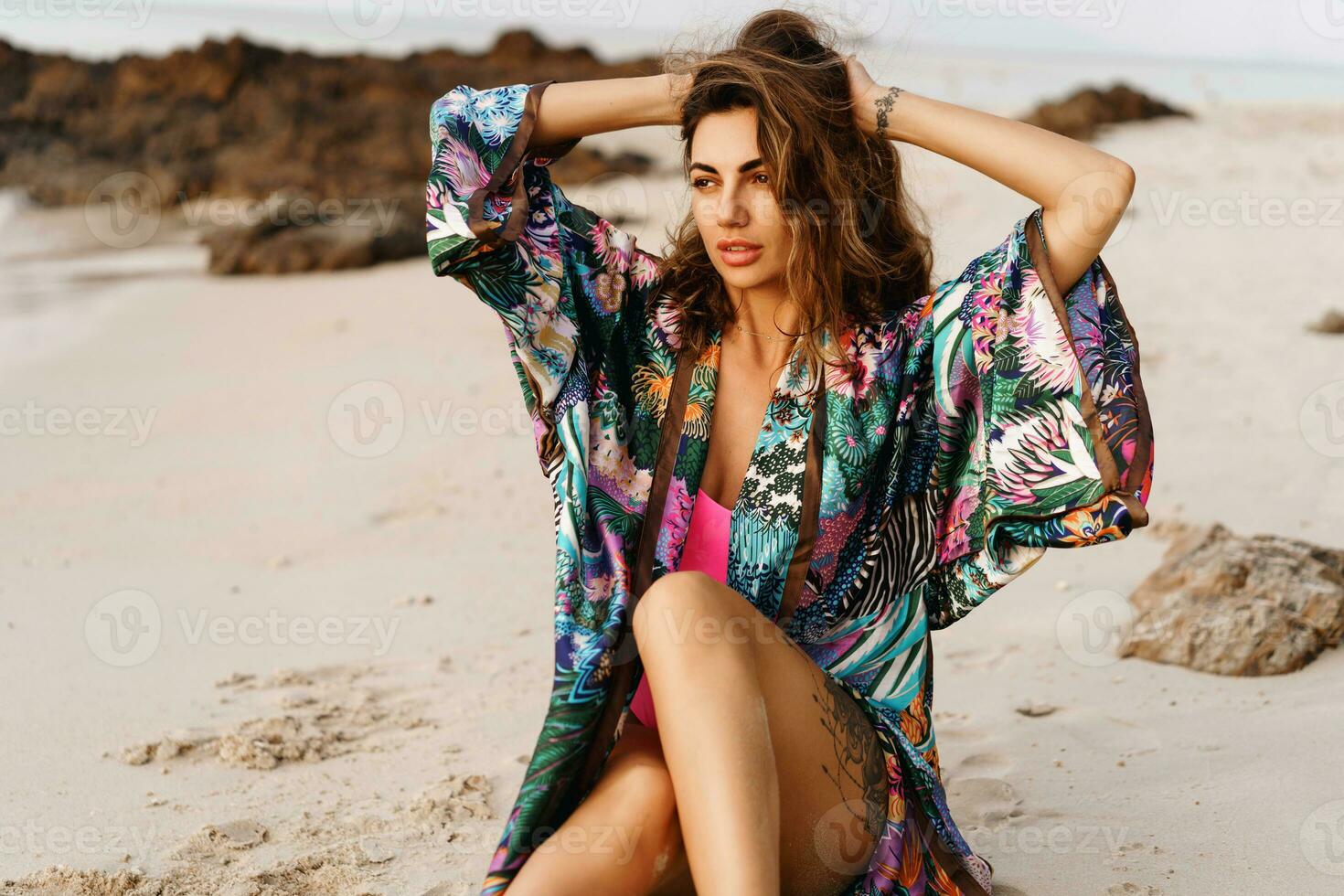 fechar acima retrato do lindo morena mulher dentro sexy roupa de banho posando em a de praia dentro pôr do sol claro. perfeito ondulado cabelos, bronzeado desnatar corpo. verão tropical humor. foto