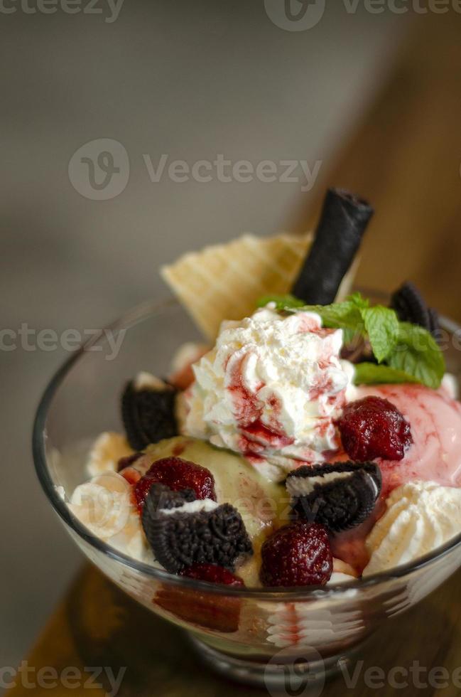 sobremesa sundae de sorvete de framboesa e pistache em uma tigela de vidro com biscoitos de chocolate e frutas vermelhas foto