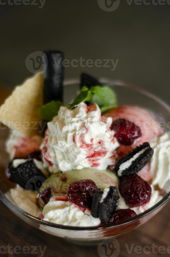 sobremesa sundae de sorvete de framboesa e pistache em uma tigela de vidro com biscoitos de chocolate e frutas vermelhas foto