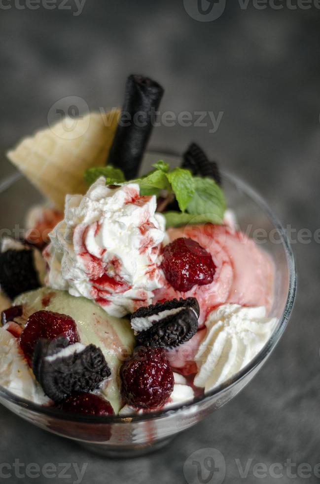 sobremesa sundae de sorvete de framboesa e pistache em uma tigela de vidro com biscoitos de chocolate e frutas vermelhas foto