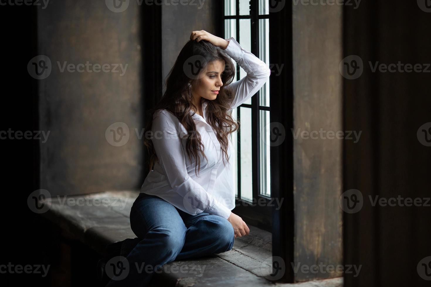 mulher de jeans senta e olha pela janela foto