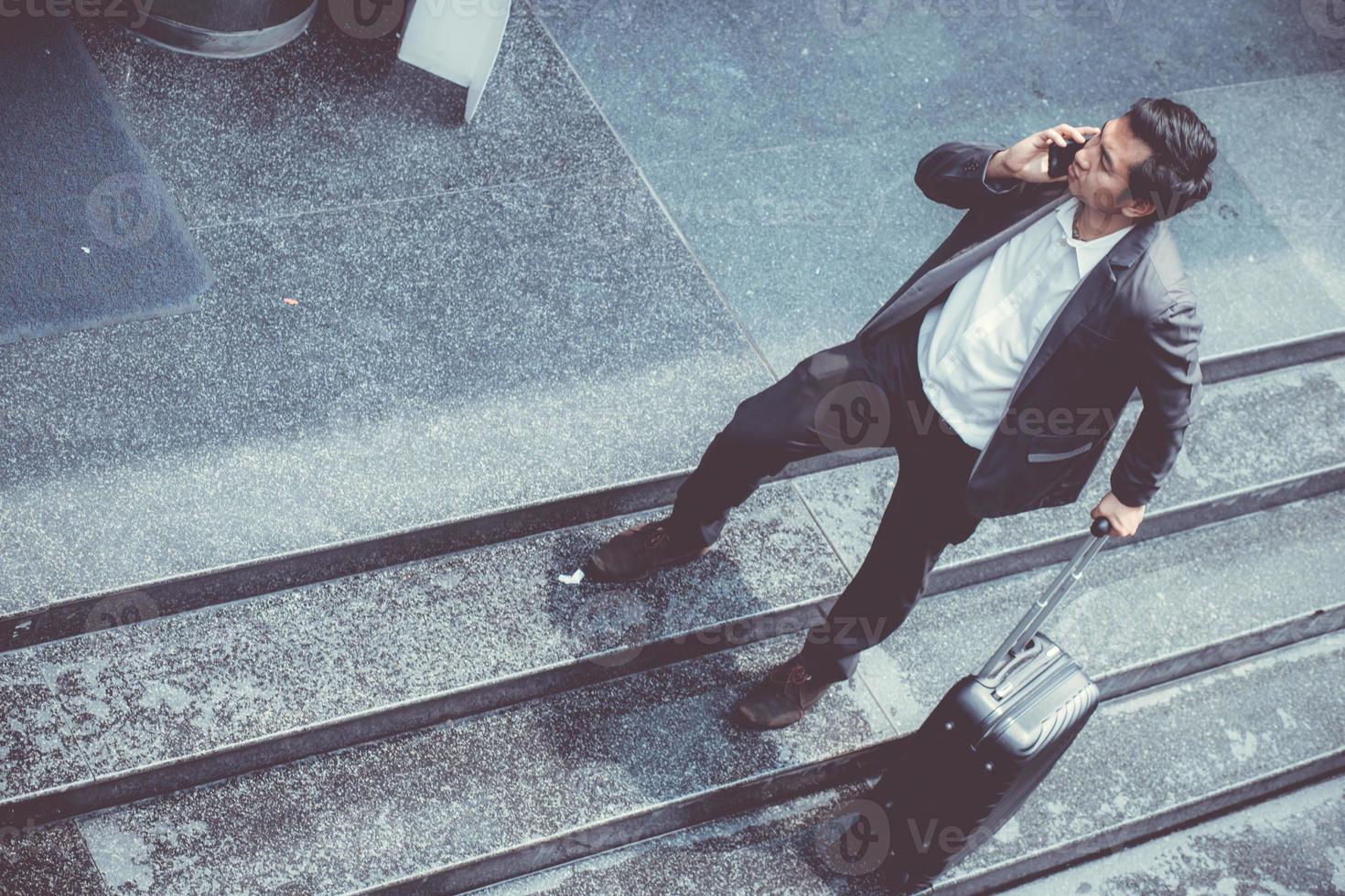 empresário asiático usar terno falando telefone enquanto segura a mala. foto