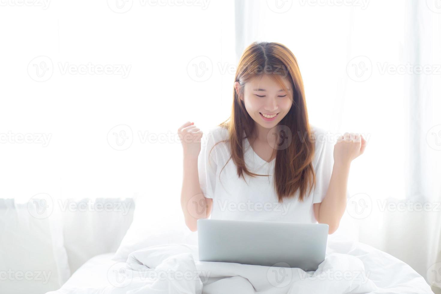 jovem mulher asiática usando laptop trabalho com sucesso na cama. foto