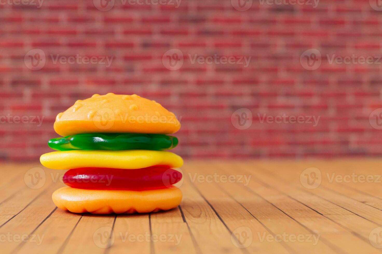 criativo disposição do grande hamburguer fez do colorida gomoso doces contra vermelho tijolo parede fundo. mínimo Comida conceito. saboroso geléia doces composição. gomoso doces estética. foto