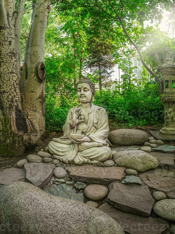 pedra gautama Buda decorativo estátua dentro uma jardim debaixo verde folhas. ao ar livre jardim decoração conceito. Abakan, vertical visualizar. foto