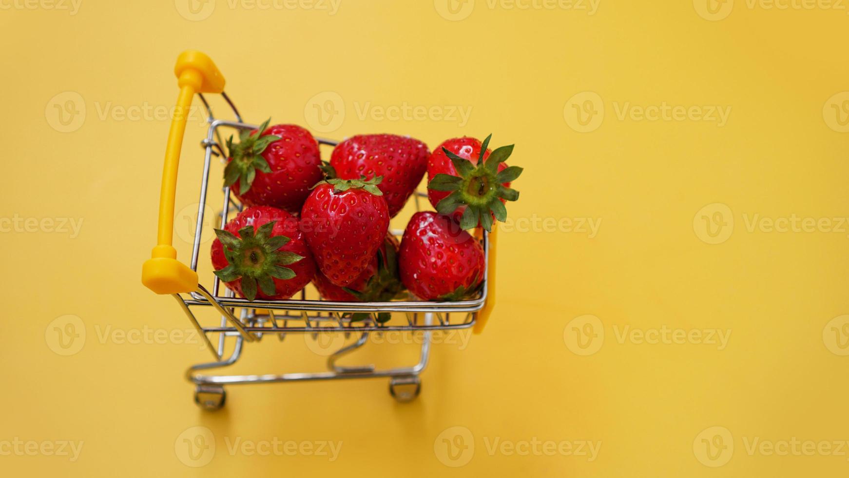 morangos frescos em um carrinho de compras em um fundo amarelo brilhante foto