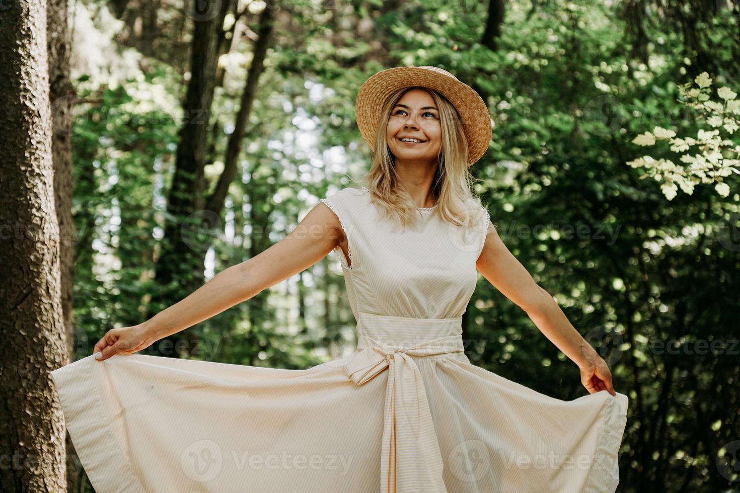 jovem com chapéu de palha segurando a bainha de seu vestido branco foto