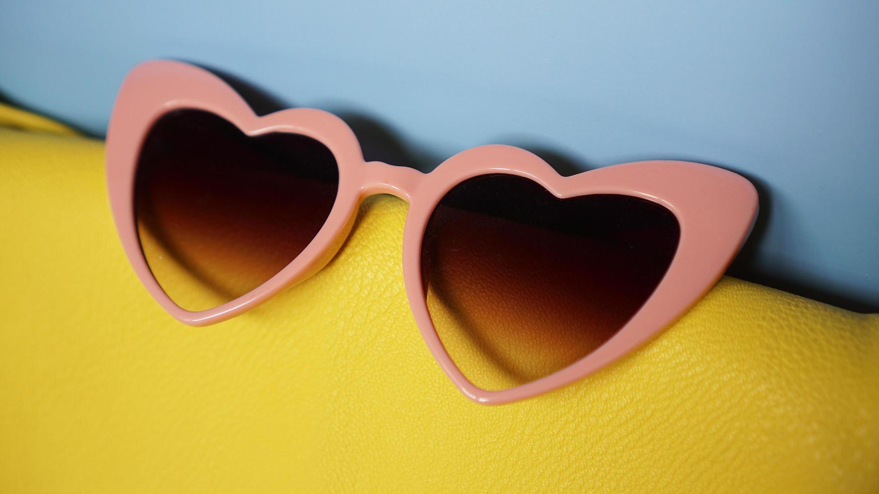 bolsa amarela e óculos de sol em forma de coração em fundo azul foto