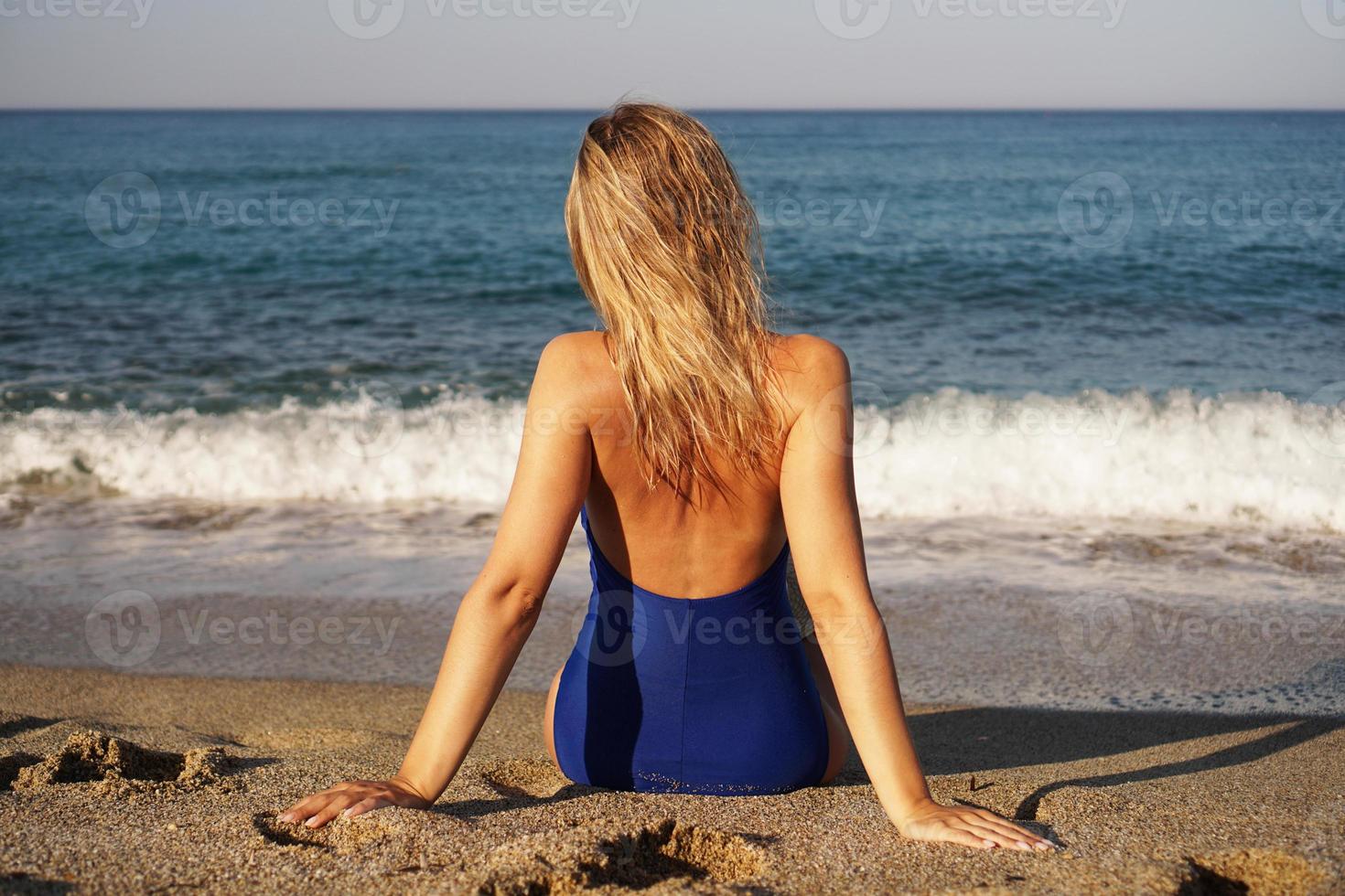 jovem tomando banho de sol na praia tropical. mulher em um maiô azul foto