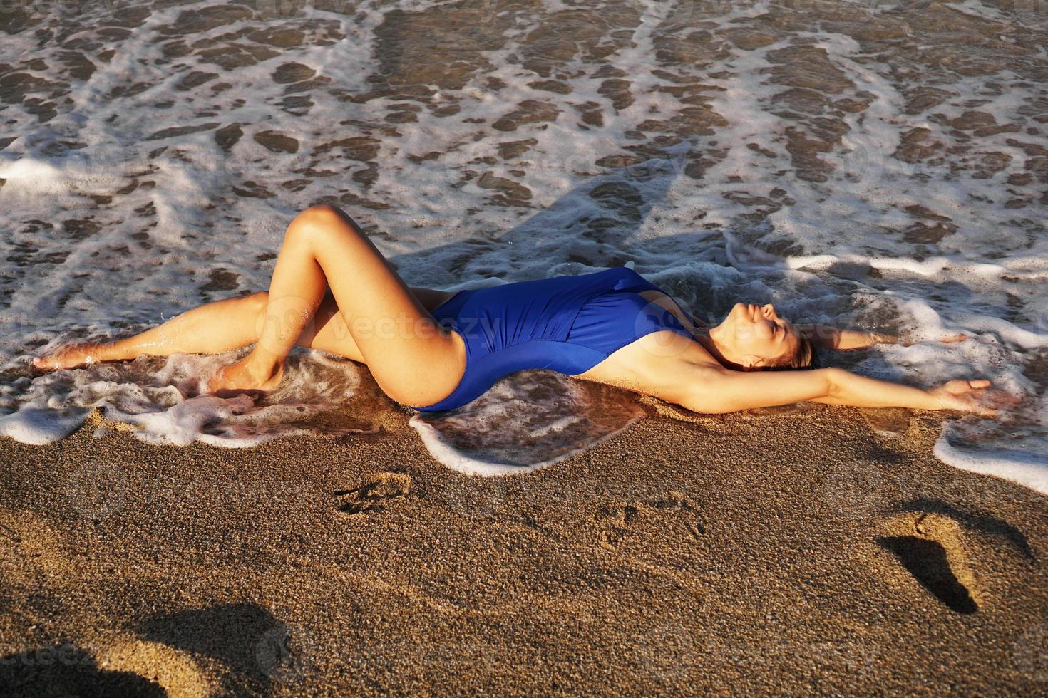 jovem tomando banho de sol na praia tropical. mulher em um maiô azul foto