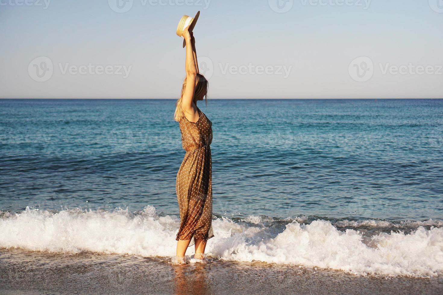 mulher na praia com um vestido marrom e um chapéu de palha foto