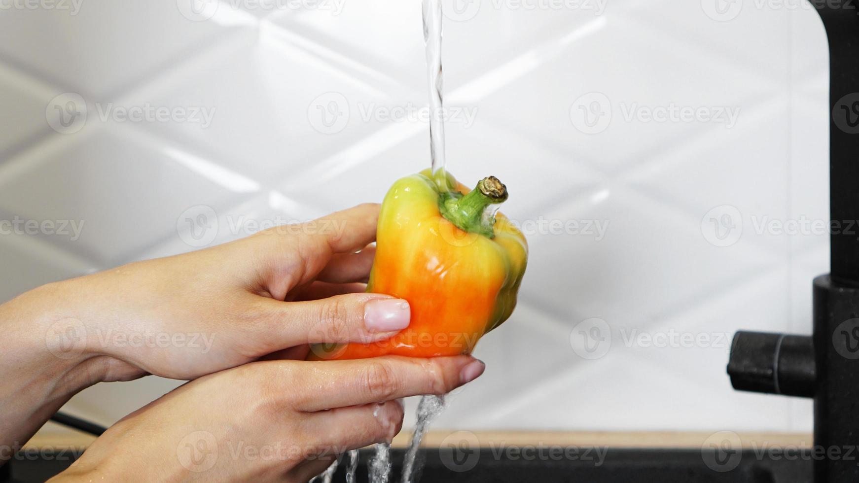 mãos femininas lavando pimenta amarela e vermelha foto