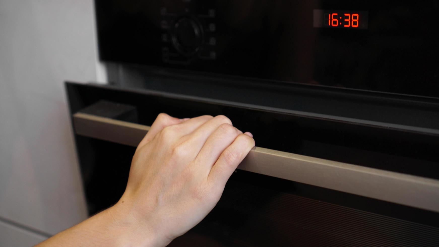 close-up da mão de uma mulher abrindo a porta do forno para controlar o assado foto