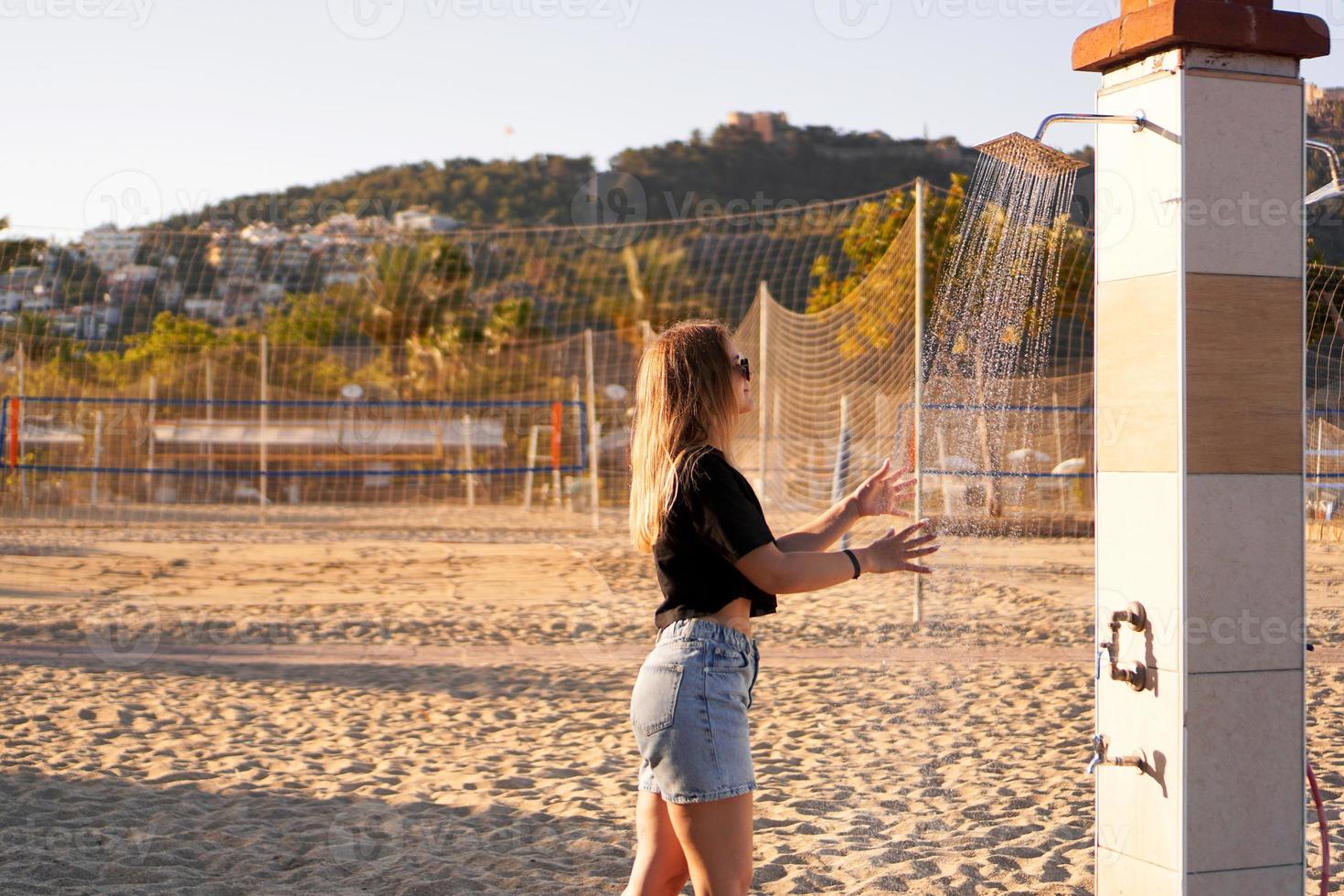 uma garota de short e uma camiseta preta na praia perto do chuveiro. foto
