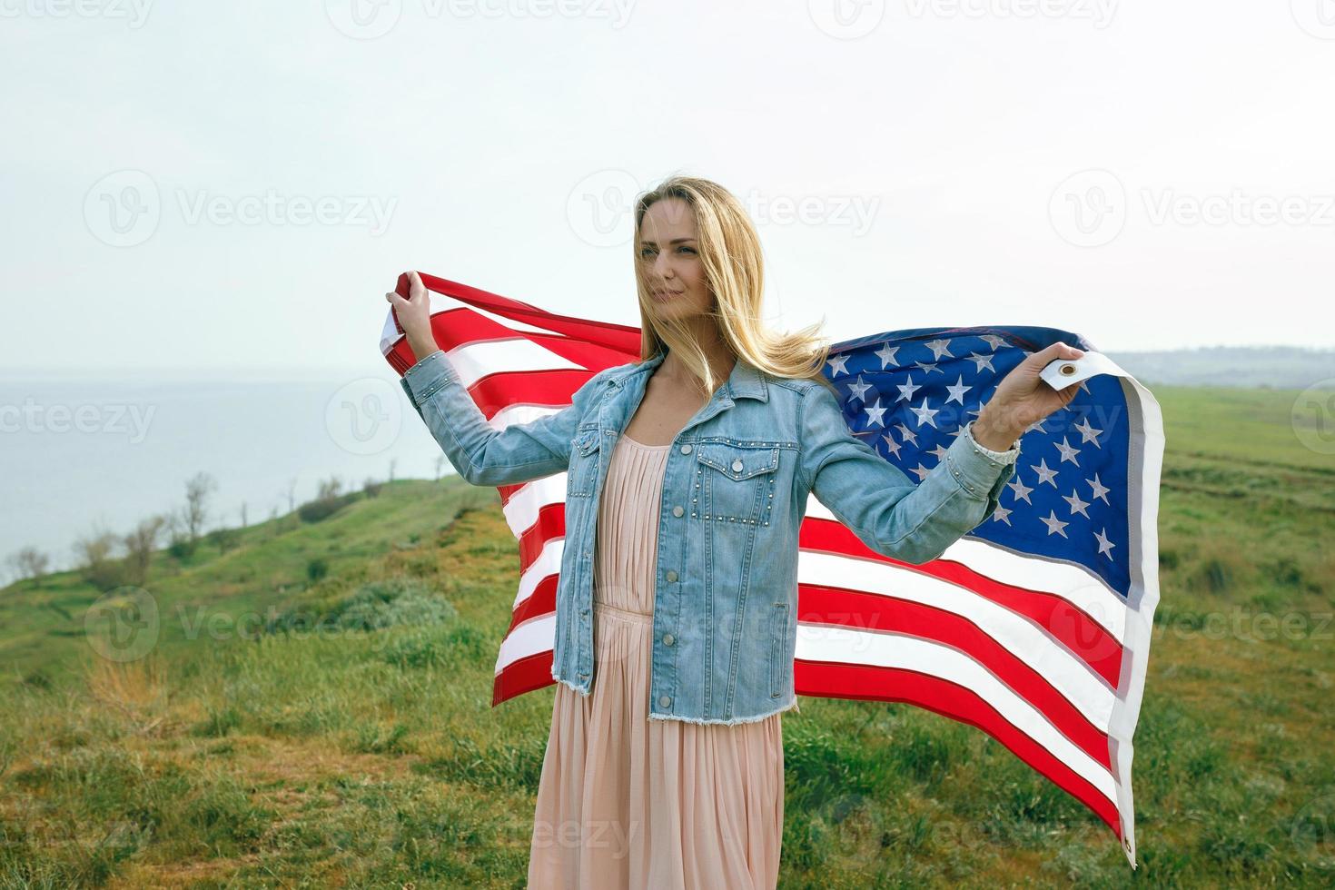 uma garota com um vestido coral e uma jaqueta jeans segura a bandeira dos EUA foto