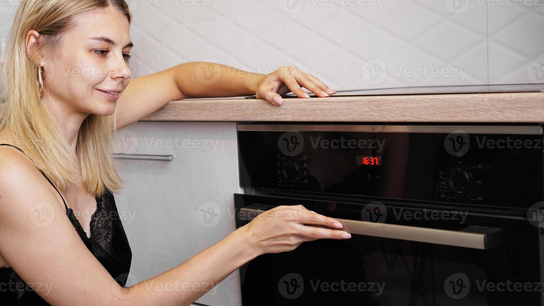 mulher cozinhando na cozinha abrindo a porta do forno foto