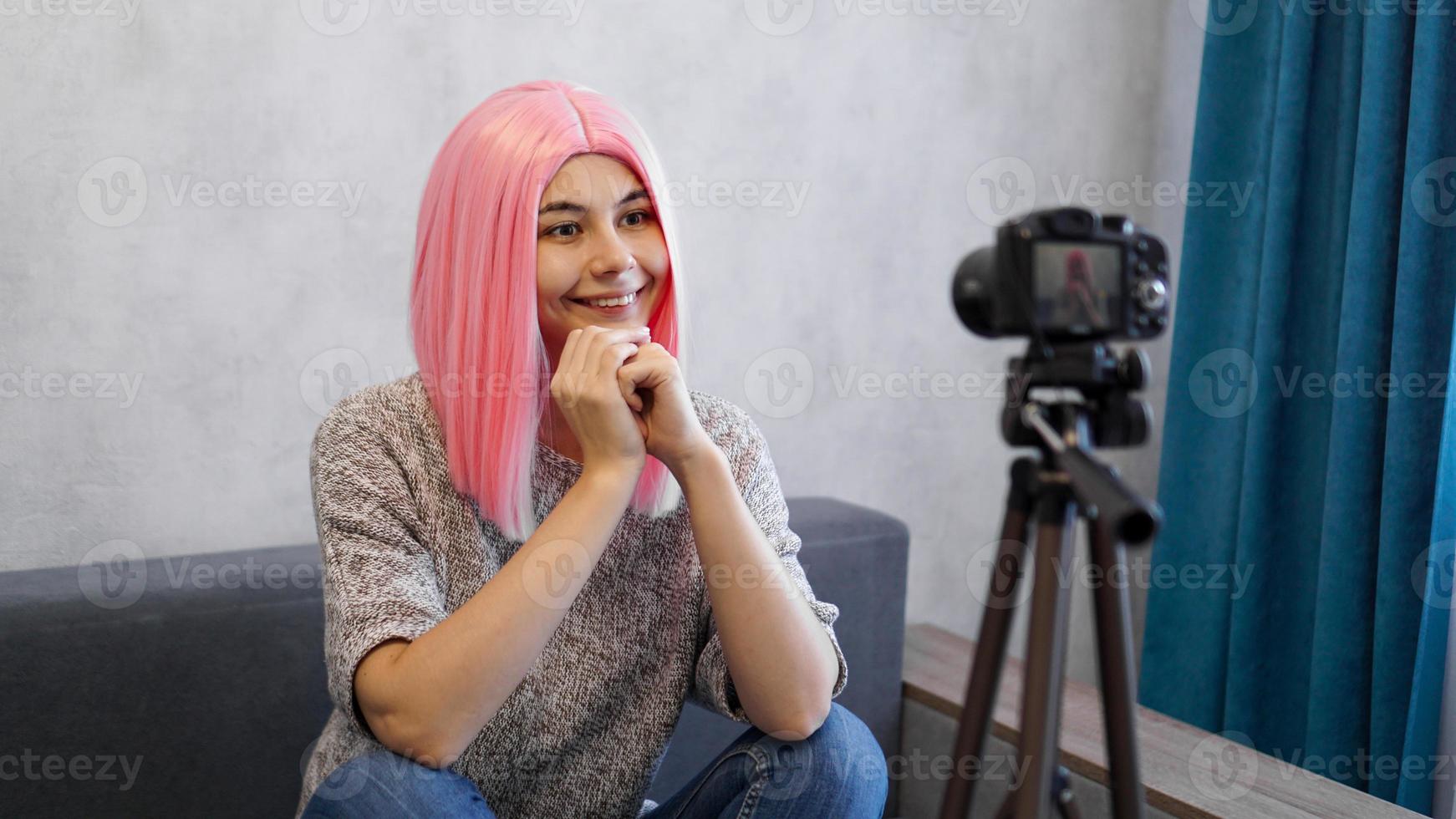 garota feliz blogueira com peruca rosa na frente da câmera em um tripé foto