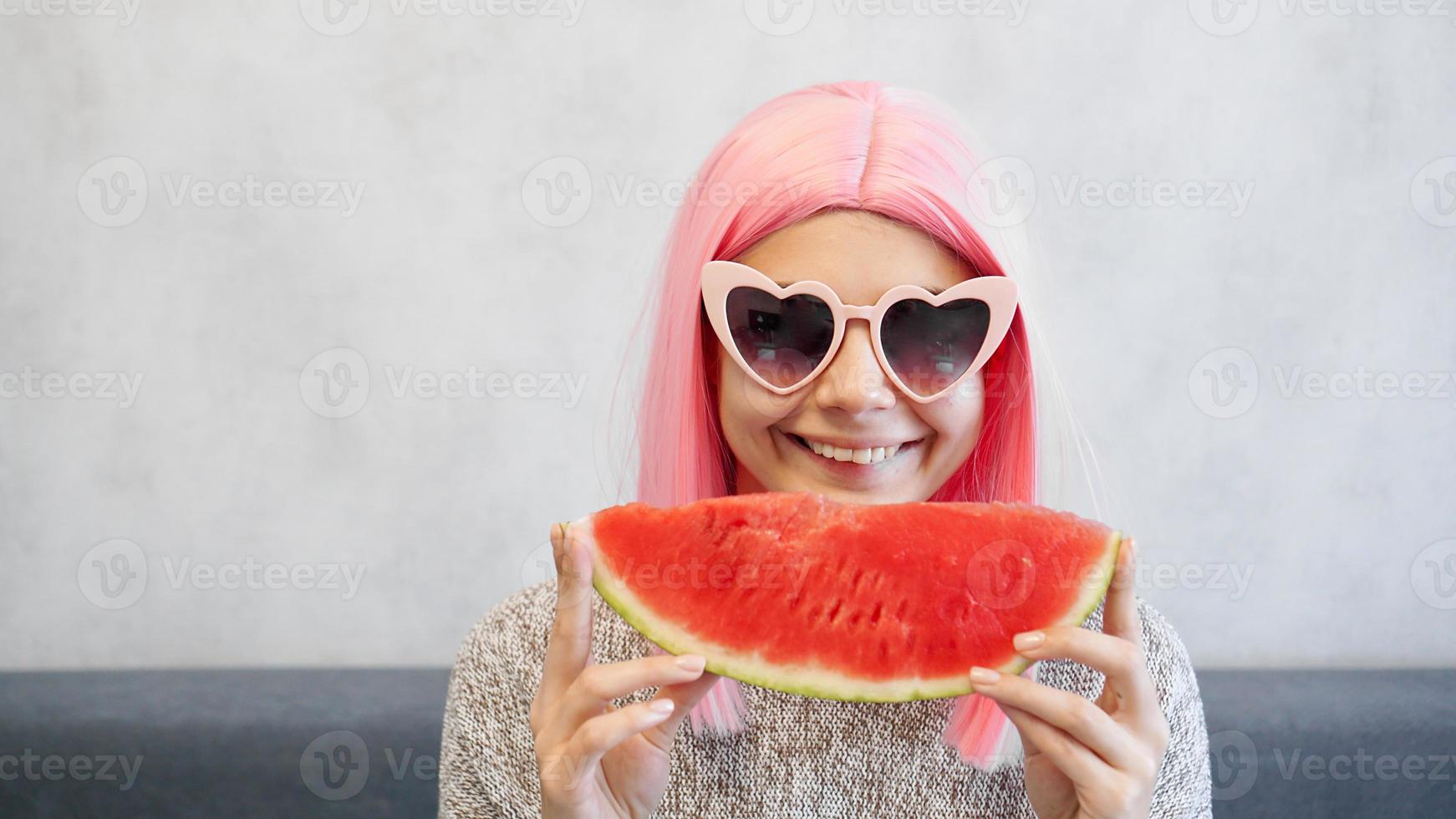 mulher com pedaço de melancia. mulher usa peruca rosa e óculos foto