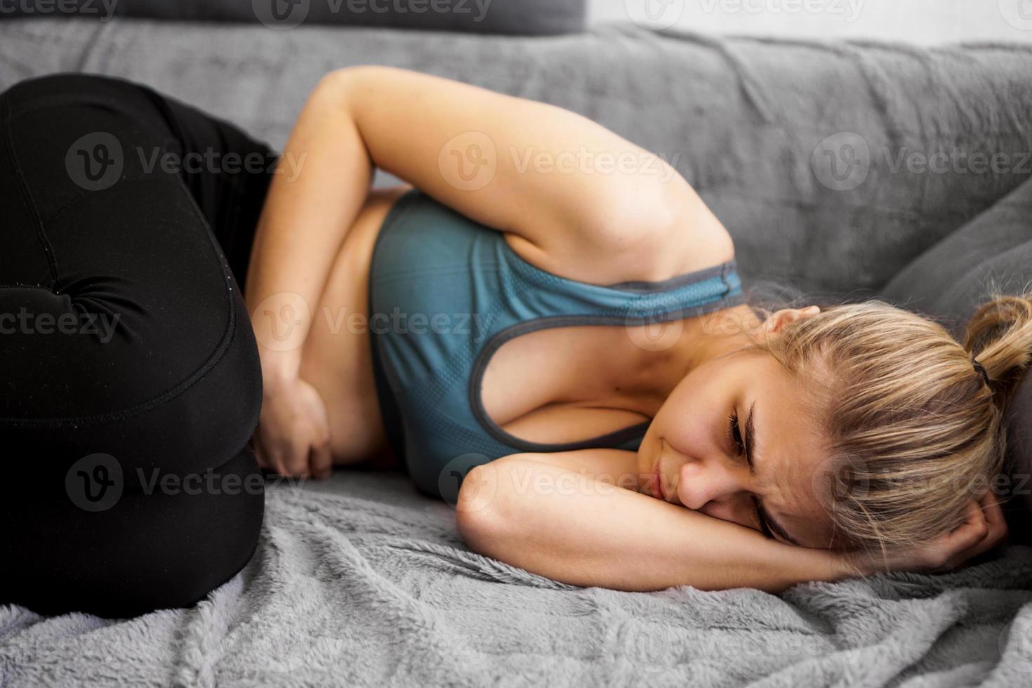 vista lateral de uma mulher com dor de estômago deitada no sofá em casa foto