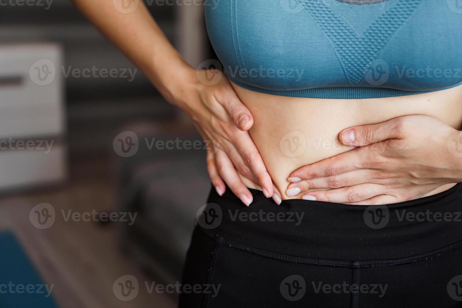 close-up da mulher segurando a barriga. dor após o treino em casa. foto