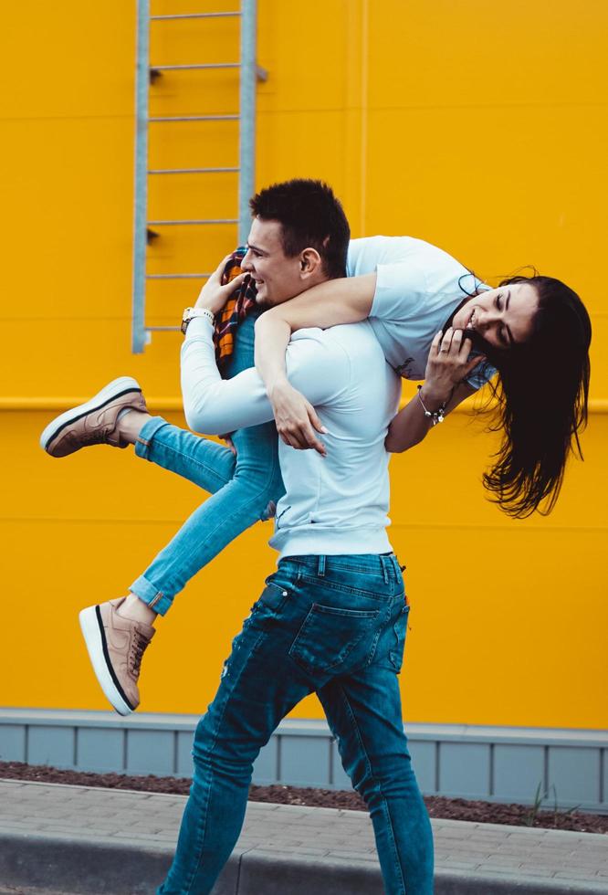 homem feliz carregando sua namorada em fundo amarelo foto