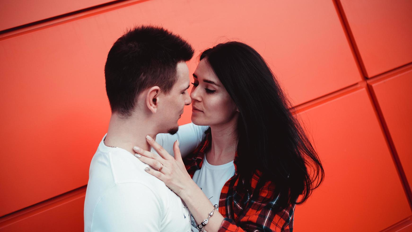 casal se beijando contra parede vermelha isolada na cidade foto