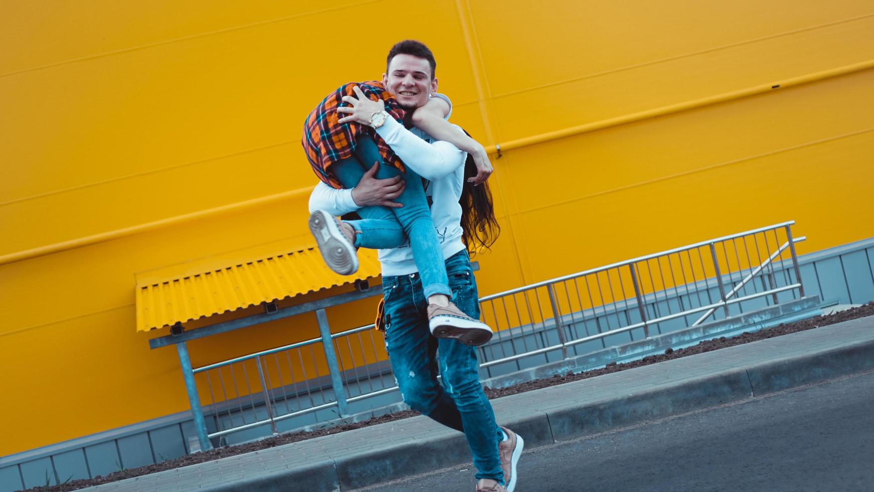 homem feliz carregando sua namorada em fundo amarelo foto