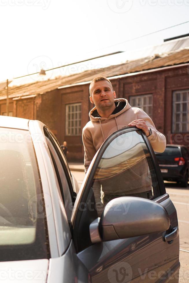 um jovem ao lado de seu carro em um dia ensolarado na rua foto