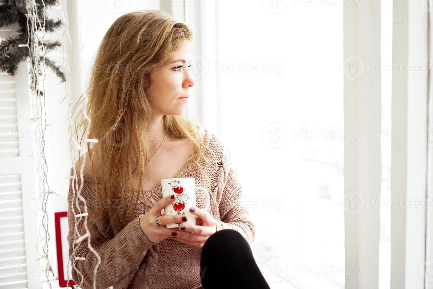 bela jovem tomando café e olhando pela janela foto