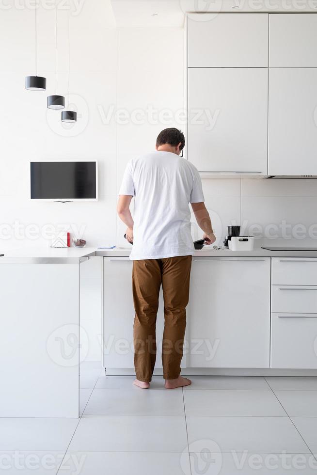 homem de camiseta branca lavando pratos na cozinha foto